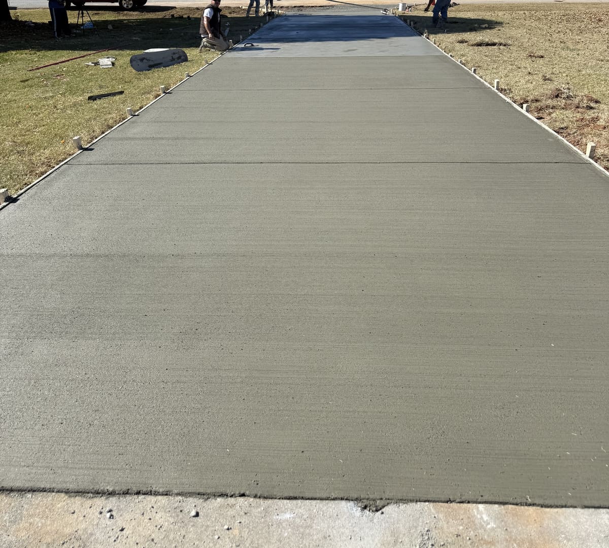Long fresh broom-finished driveway between wood forms, crew finishing the far end
