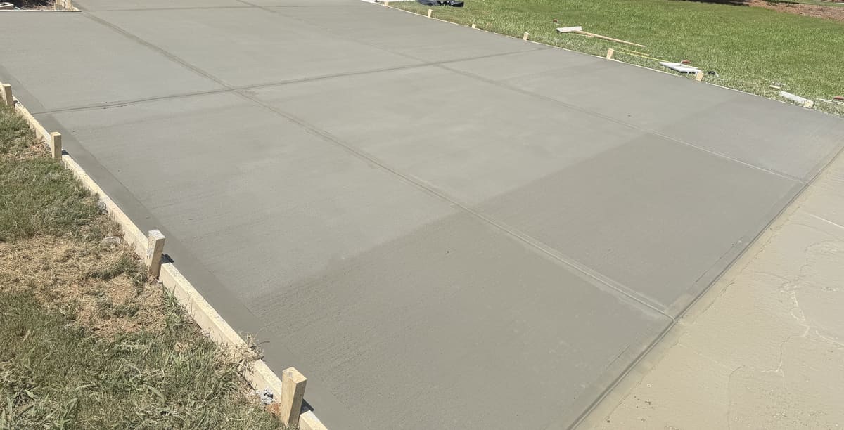 Fresh broom-finished driveway with control joints between wood forms, a lawn along one side