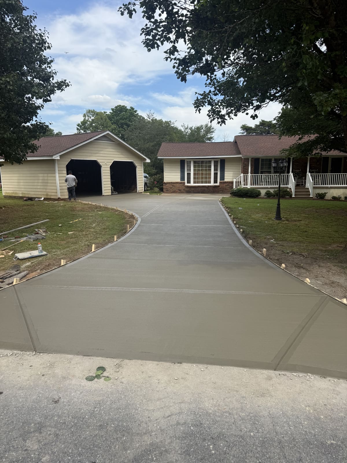 Fresh driveway curving from the road to a detached two-car garage and a brick house with a white-railed porch