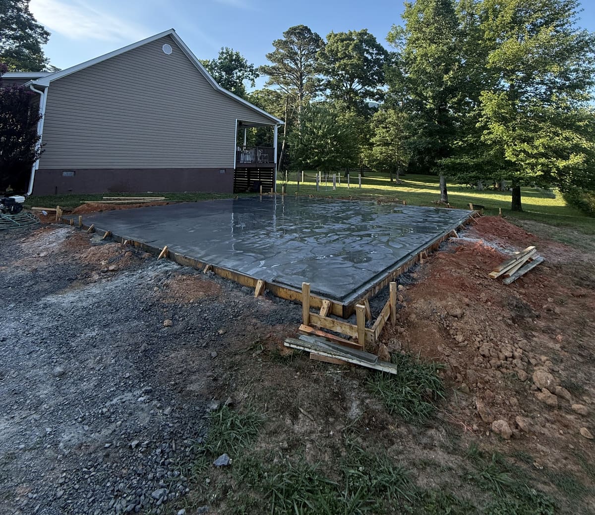 Fresh pad inside wood forms beside a tan house with a covered side porch, its surface still wet