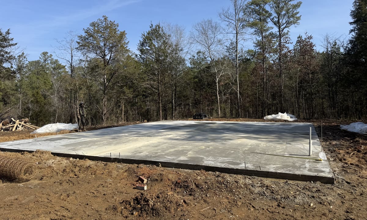 Cured pad in cleared woods with white plastic sheeting and a roll of wire mesh nearby, a crew member at the far edge