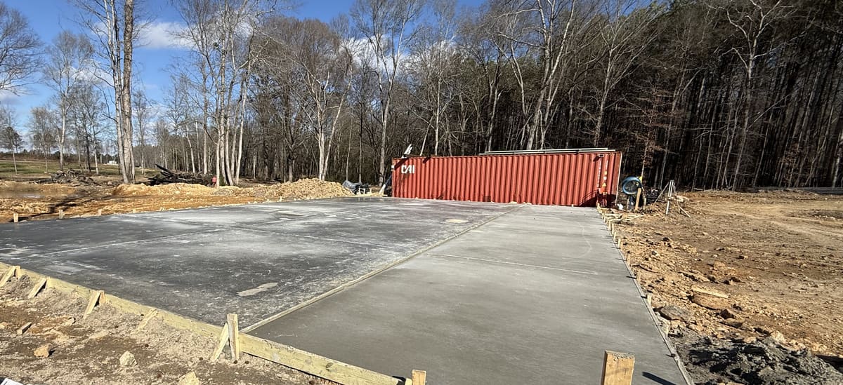 Fresh pad in wood forms with control joints, bare trees and a red shipping container behind