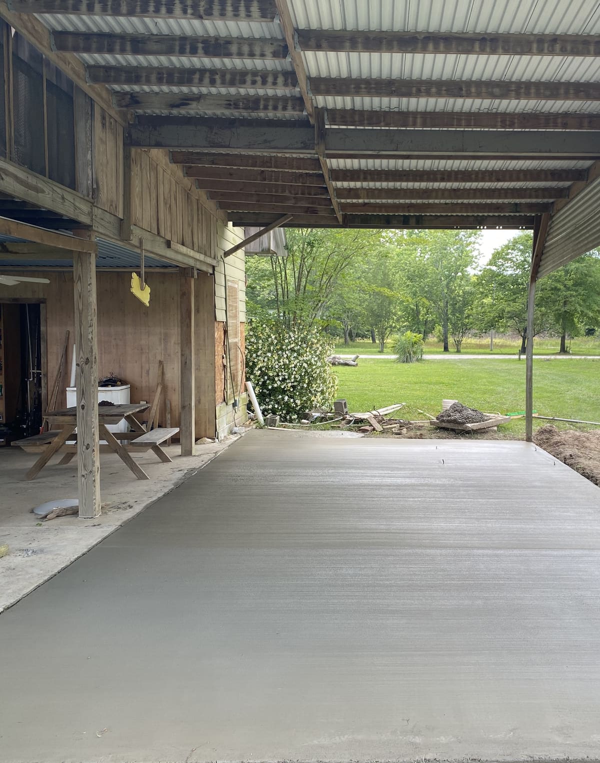 Fresh broom-finished slab under a metal-roofed lean-to on a wooden barn, an older slab with a picnic table beside it