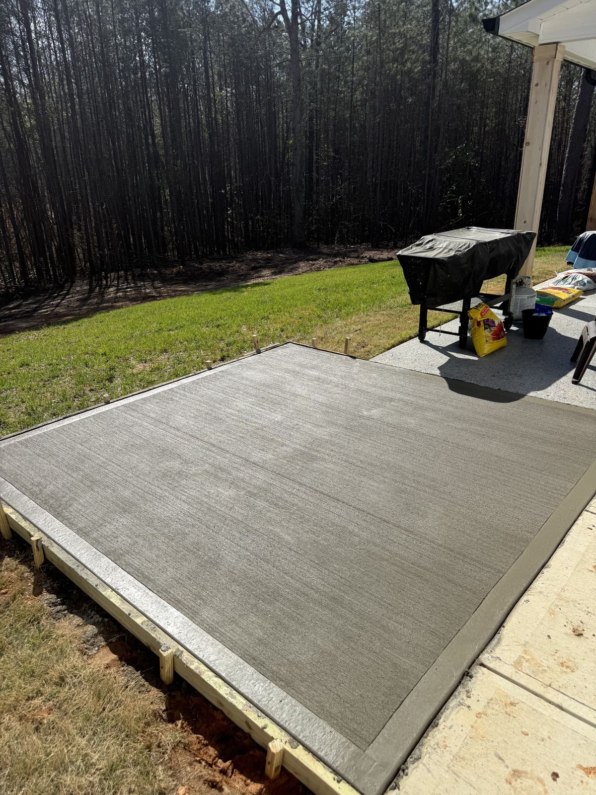 Patio extension in wood forms off a covered porch, broom finish with a smooth troweled border, pine woods beyond