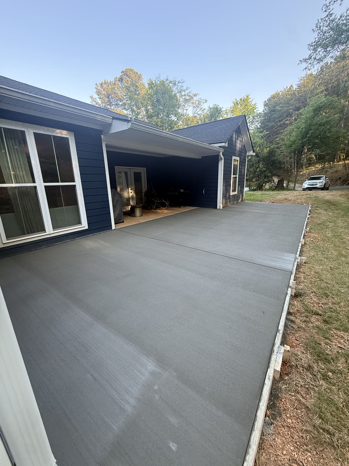 Broom-finished patio slab with control joints along a navy blue house and its covered porch