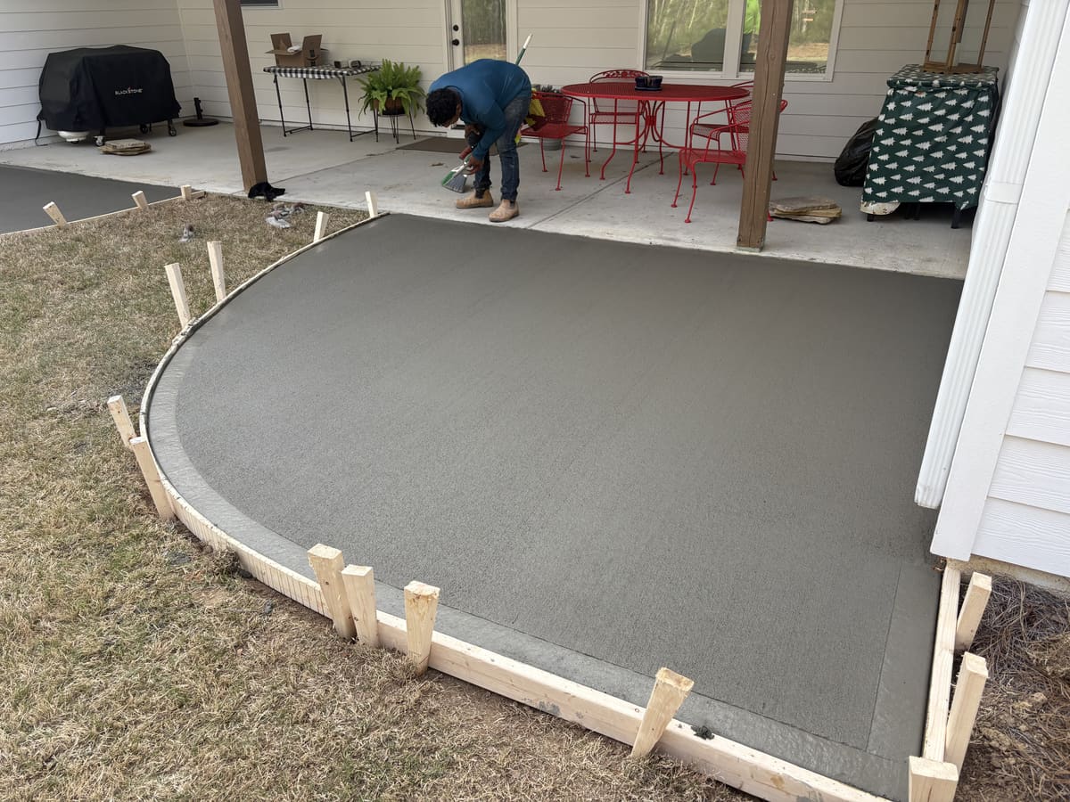Fresh curved patio extension with a smooth troweled border in wood forms, off a covered porch with red chairs