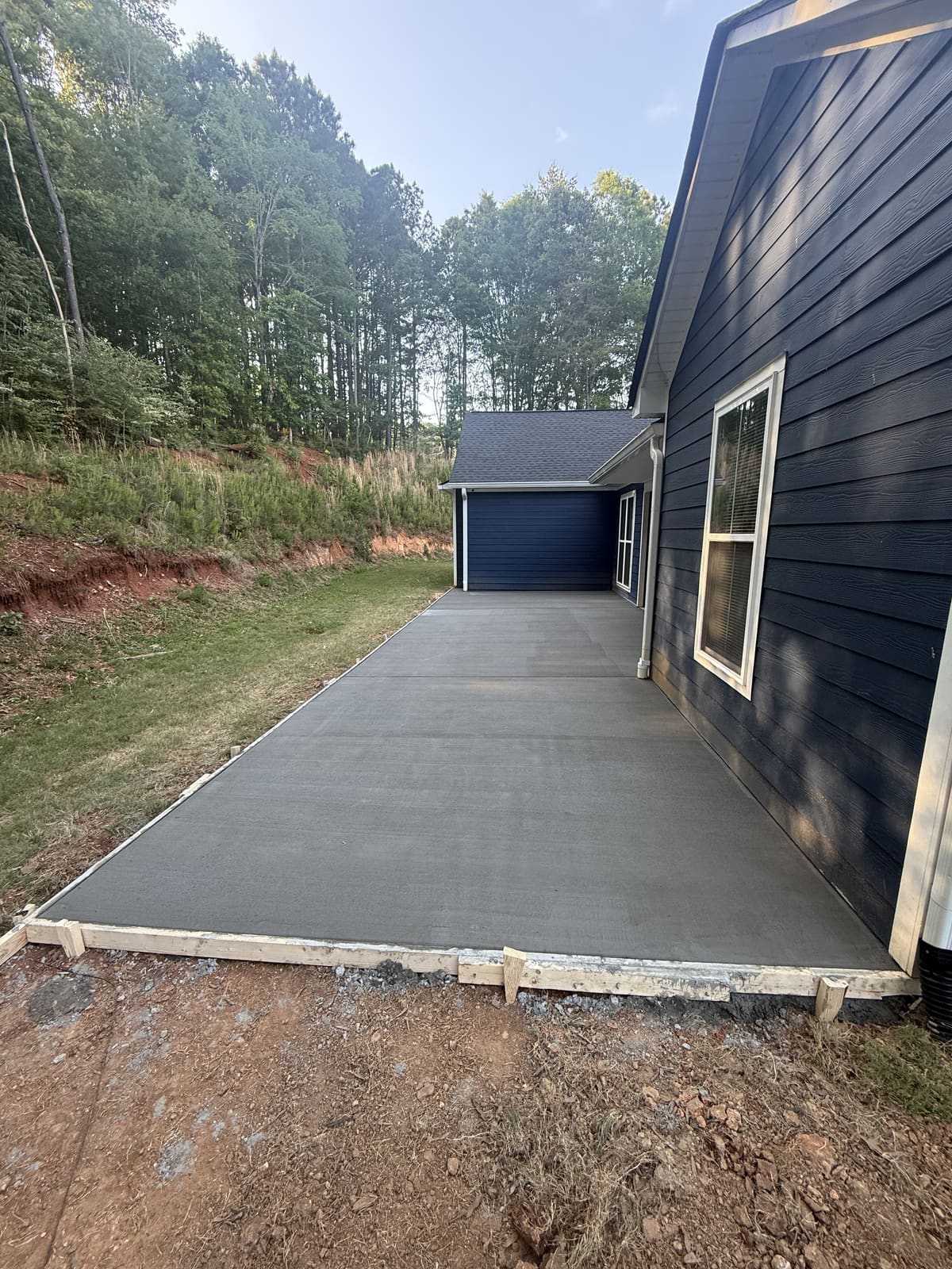 Broom-finished slab with control joints along the side of a navy blue house, wood forms on the front edge