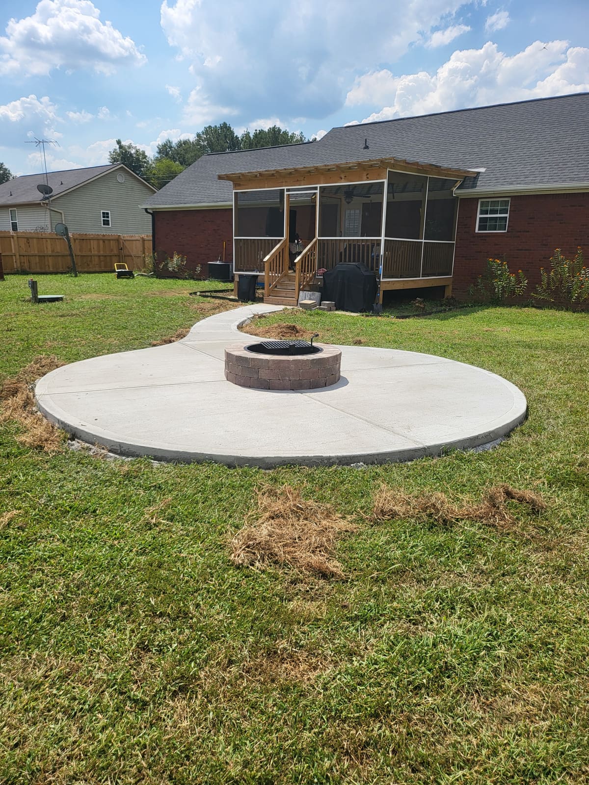 Round concrete patio with a stone fire pit at its center and a curved walkway to a screened back porch