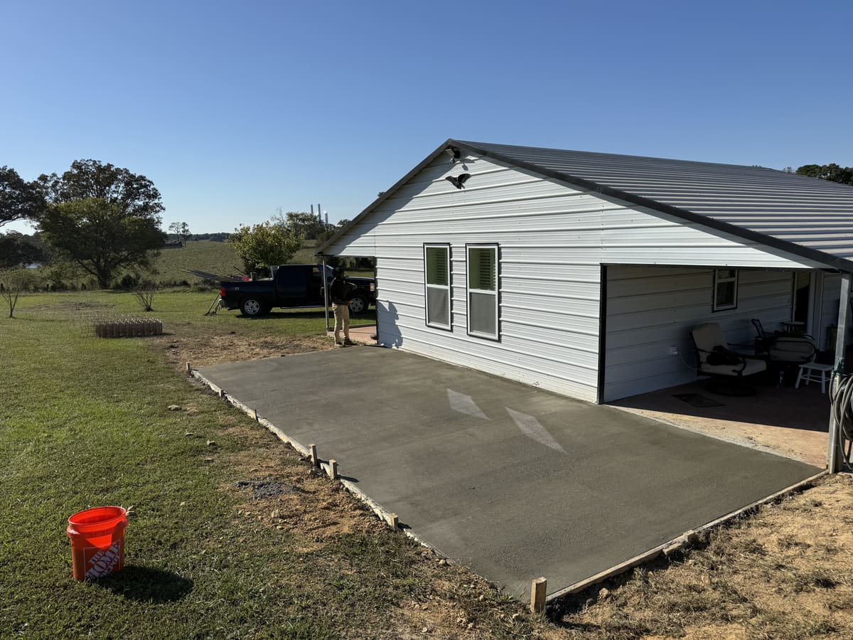 Fresh broom-finished slab along a white metal-sided building with a covered porch, open pasture beyond