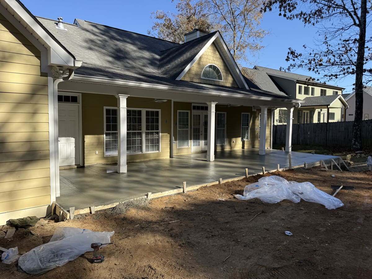 Freshly poured slab, still wet, under a long covered back porch with white columns on a yellow house