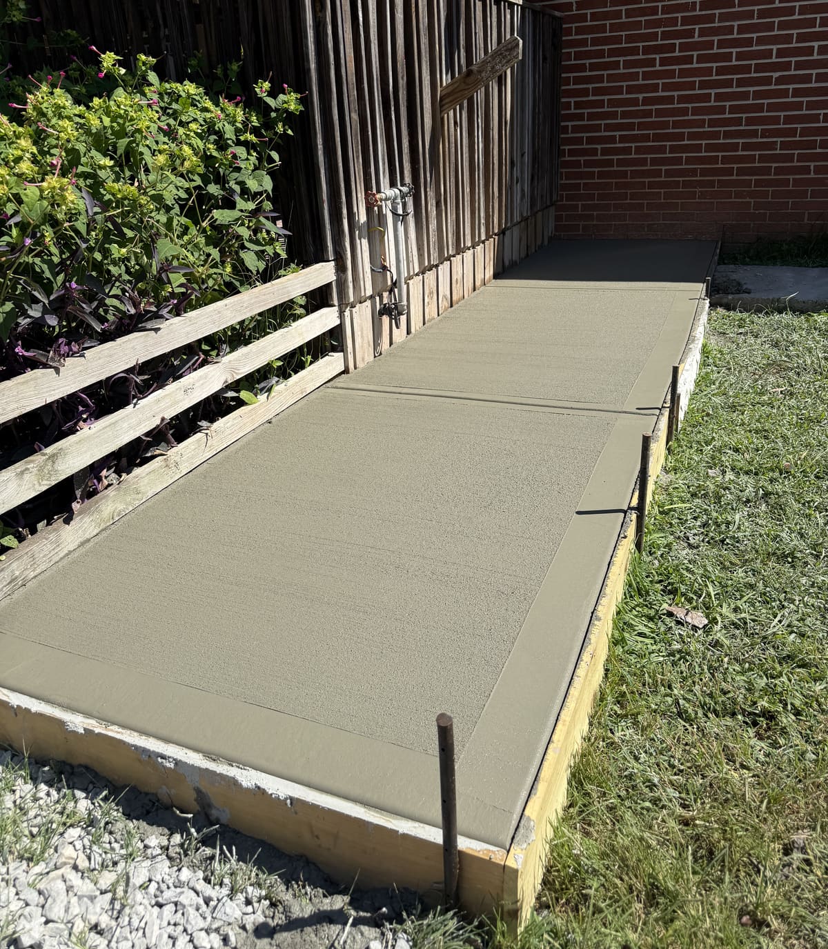 Fresh broom-finished walkway with a smooth troweled border along a wood privacy fence, forms and stakes in place