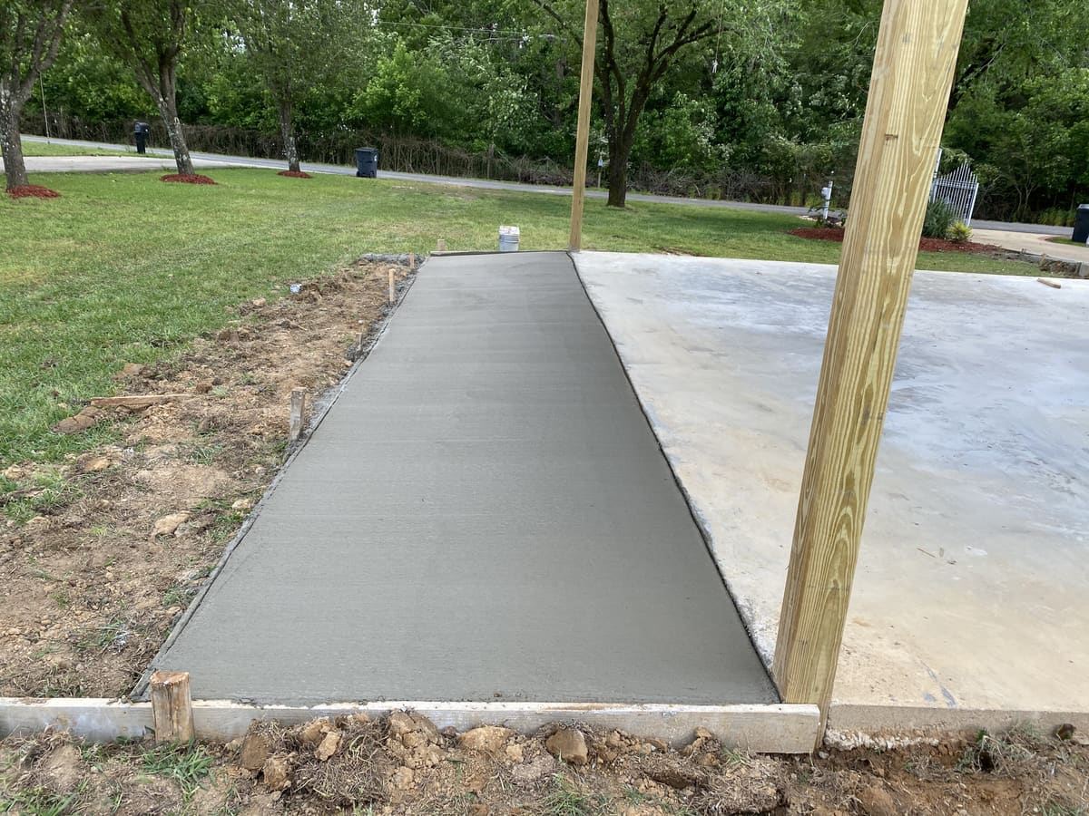 Fresh broom-finished concrete strip poured along an existing slab, wood forms and a treated post beside it